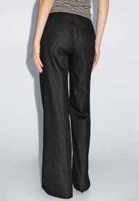 Zwarte denim wijde broek met een gladde textuur, voorzien van achterzakken en een rechte snit. Zichtbare stikseldetails accentueren het ontwerp.