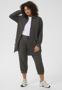 Camicia leggera grigio scuro con bottoni e tasca, indossata sopra una maglietta bianca e abbinata a pantaloni cropped coordinati. Tessuto strutturato.