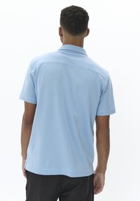Polo shirt azzurro chiaro a maniche corte con colletto, texture liscia e orlo dritto, caratterizzato da un design a yoke nella parte posteriore.