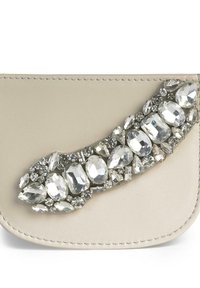 Clutch in pelle beige con un design arrotondato e abbellimenti, caratterizzato da un insieme di strass trasparenti e gemme di forme diverse lungo un lato.