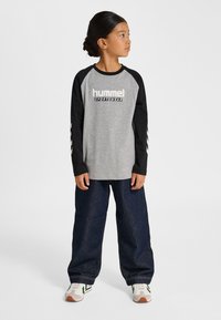 Grå långärmad tröja med svarta ärmar och "hummel sportswear"-logga. Bärs med lös mörk denimjeans och vita sneakers.