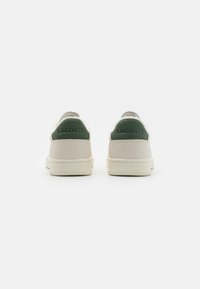White leather sneakers with green accents on the heel. Features a smooth texture and subtle raised lettering. Low-top design with minimal stitching.