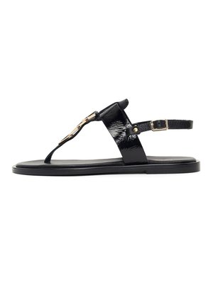 Sandalo piatto in pelle verniciata nera con cinturino alla caviglia, anello per l'alluce e fibbia decorativa color oro su sfondo bianco.