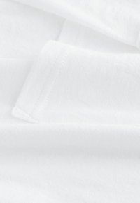 Tessuto di cotone bianco con una texture morbida e liscia; presenta cuciture sottili e una qualità leggera e traspirante.
