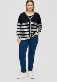 Námořnický pruhovaný cardigan s krémov�ými akcenty, zapínání na knoflíky a jemnou texturou. Nosený přes tmavý top s modrými džíny a bílými teniskami.
