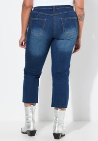 Tummansininen farkkuhousut, joissa on istuva muotoilu, risat helmat ja kaksi takataskua. Yhdistetty hopeisiin nilkkureihin.