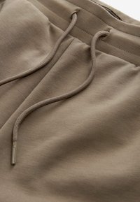 Pantalons de jogging en coton beige avec cordon de serrage, présentant une texture lisse et des détails de couture subtils.