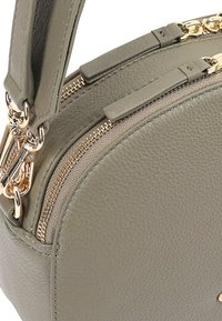 Ronde olijfgroene leren handtas met een gestructureerde afwerking, voorzien van gouden ritsdetails en een korte, platte handgreep.