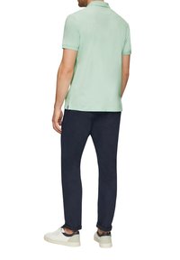 Jasnozielona koszulka polo z krótkimi rękawami, w zestawie z ciemnonawowymi spodniami i białymi trampkami z granatowymi akcentami. Gładka tekstura materiału.