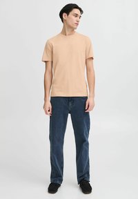 Beige crew neck t-shirt paired with dark blue straight-leg jeans. The t-shirt features short sleeves and a relaxed fit.