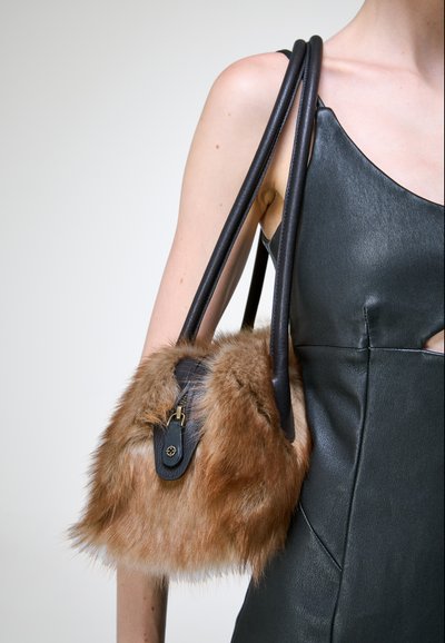 Personne portant une robe en cuir noire sans manches, portant un sac à main en fausse fourrure marron avec de longues bretelles en cuir noir sur l'épaule.