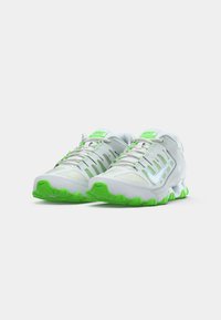 Nike futócipők fehér felsőrésszel, neon zöld kiegészítőkkel és texturált talppal. Karcsú dizájnnal és csíkos oldalrészletezéssel rendelkezik.