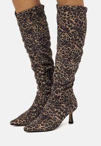 Botas hasta la rodilla con estampado de leopardo, textura de tela suave, diseño de punta puntiaguda y tacón delgado. Presentan fruncido y cremallera lateral.