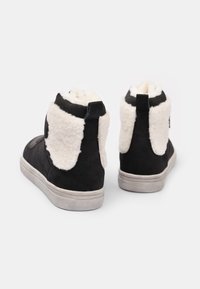 Svarta mocka ankboots med vit fluffig foder, kontrasterande svart kant och en grå gummisula. Har en bakre dragflik för enkel påtagning.