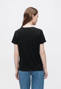 Čierne bavlnené tričko s uvoľneným strihom, krátkymi rukávmi a okrúhlym výstrihom, v páre so svetlomodrými džínsami s vysokým pásom.