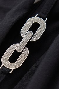 Zilverkleurige schakelhardware met steentjes, bevestigd op een zwarte stoffen achtergrond, met een gladde textuur en gedurfde geometrische vorm.