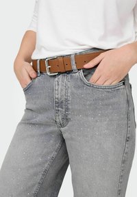 Jeans de mezclilla gris con detalles dispersos de pedrería, cintura alta, botón de metal y trabillas para cinturón, combinados con un cinturón de cuero marrón y una blusa blanca.