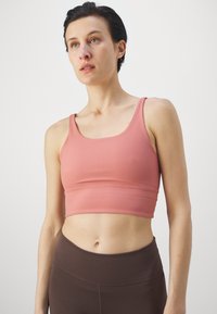 Ριγέ ροζ αθλητικό σουτιέν με φαρδιές τιράντες και εφαρμοστή σχεδίαση, συνδυασμένο με καφέ ψηλόμεσα κολάν. Λείος υφασμάτινος χαρακτήρας με ελάχιστες ραφές.