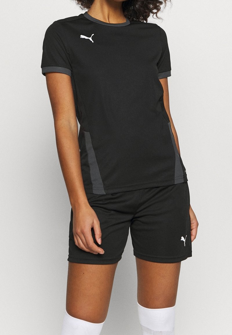 Ensemble de sport noir comprenant un haut à manches courtes et un short, fabriqué à partir de matériau respirant avec des accents gris sur les côtés et des détails de logo blancs.