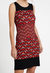 Robe sans manches à motifs rouges et noirs, présentant un design géométrique avec un corsage ajusté et une jupe noire unie. Tissu texturé.