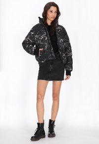 Pufferjack met een zwart marmerpatroon, ritssluiting, zijzakken, gecombineerd met een zwarte spijkerrok en zwarte combatlaarzen.