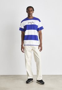 Camiseta a rayas azul y blanca con el logotipo bordado "Tommy Jeans", combinada con pantalones color crema y zapatillas negras. Diseño sencillo, ajuste informal.