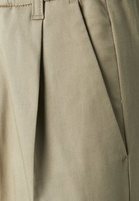 Dettaglio ravvicinato di tessuto beige con cuciture dettagliate e un passante per cintura su un indumento plissettato.