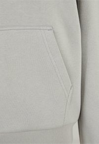 Gros plan d'une poche de sweat à capuche gris clair avec des coutures visibles et un ourlet côtelé au bas du vêtement.