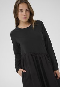 Fekete, hosszú ujjú ruha, szűkített fazonú felsőrésszel és fodros, texturált szoknyával, zsebekkel, sima felülettel és réteges kialakítással.