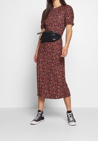 Květinové midi šaty s nabíranými rukávy, červeno-černý vzor, doplněné černou síťovanou ledvinkou a černými vysokými teniskami.