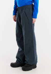 Mörkgrå vattentäta byxor har elastisk midja med ett bälte, en figursydd design och textil som ger hållbarhet. Svarta stövlar fulländar looken.