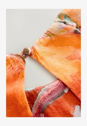 Tessuto testurizzato arancione con motivi floreali. Presenta un collo rotondo e una chiusura con bottoni sul retro, evidenziando dettagli intricati.