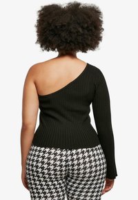 Félvállas fekete bordás top, az egyik oldalon hosszú ujjú, testhez simuló szabással. Fekete-fehér kutyafog mintás leggings-szel párosítva.