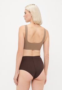 Brown bra top with wide straps; smooth texture, square back. Paired with high-waisted brown briefs featuring a seamless design.