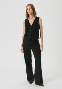 Black pinstripe two-piece outfit featuring a sleeveless vest with five buttons and wide-leg trousers, both made of textured fabric.