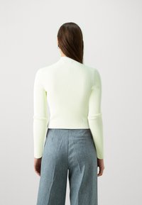 Geribbeld, lang mouwtop in lichtgroen met een hoge hals, gecombineerd met hoge taille, wijde spijkerbroek met een zijzak.