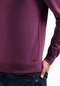Paars gebreid sweater met een geribbelde onderrand en manchetten, voorzien van een klein zwart label aan de onderzijde links. Zachte textuur, aansluitend ontwerp.