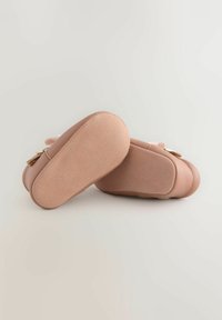 Pink leather baby shoes with rounded toes, soft soles, and a textured finish. Metallic accents and a buckle detail on the side.