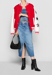 Chaqueta varsity roja y blanca con detalles de estrellas, combinada con una falda de mezclilla con abertura frontal, botas de tacón negras y un bolso negro.