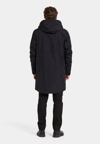Svart vattentät parkas med huva, med en midjelång design, slät textur och rak skärning, kombinerad med svarta byxor och skor.