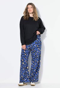 Sweatshirt noir oversize à manches longues associé à un pantalon large bleu avec un imprimé léopard en accents noir et beige.
