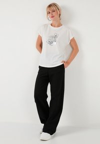 Hvid t-shirt med korte ærmer og blomsterdesign i stregtegning, parret med sorte vide bukser og hvide sneakers. Enkel, afslappet påklædning.