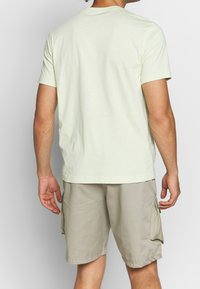 Světle zelené bavlněné tričko s krátkým rukávem, kulatým výstřihem a hladkouTexturou, spárované s béžovými cargo šortkami s bočními kapsami.