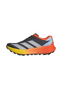 Chaussure de sport noire, grise et orange avec semelle jaune, design à lacets et marquage "Terrex" sur le talon, conçue pour la course sur sentier.