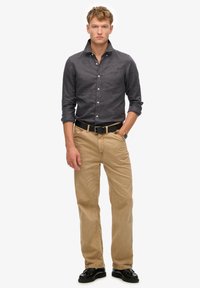 Camisa abotonada de color gris oscuro combinada con chinos beige claros. Cinturón de cuero negro y zapatos negros brillantes. Diseño simple y estructurado sin patrones.