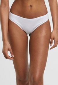 Vit bomullsbikini med slät textur, låg midja och enkel elastisk midjeband, som framhäver en minimalistisk estetik.