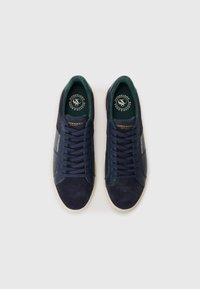 Navy blue sneakers made of suede and synthetic material, featuring rounded toes, rubber soles, and green fabric lining with logo details.