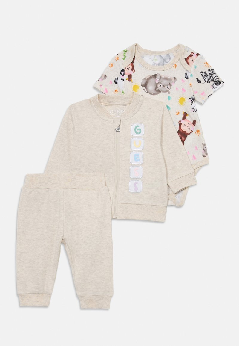 Dreiteiliges Babykleidung. Beigefarbene Zip-Jacke mit "GUESS" Schriftzug, passende Hose und ein farbenfrohes Tiermuster-Body. Aus weichem Baumwollmaterial.