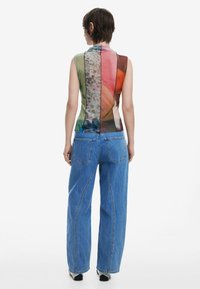Sleeveless multicolored top featuring a mix of floral and abstract patterns, paired with loose blue denim jeans and split-color design.