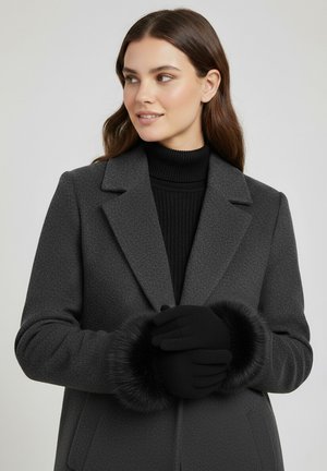 Gray wool coat with a structured design, featuring a textured finish and black fur cuffs. Worn over a black ribbed turtleneck and black gloves.